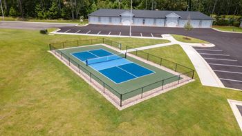 A tennis court is surrounded by a parking lot and a building.